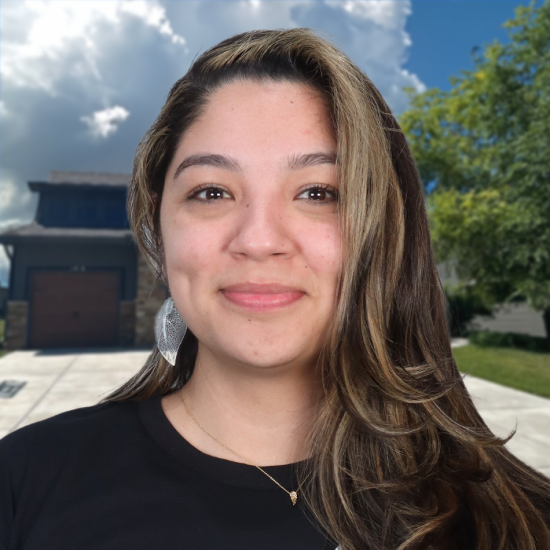Smiling woman in front of a house with a cloudy sky background.