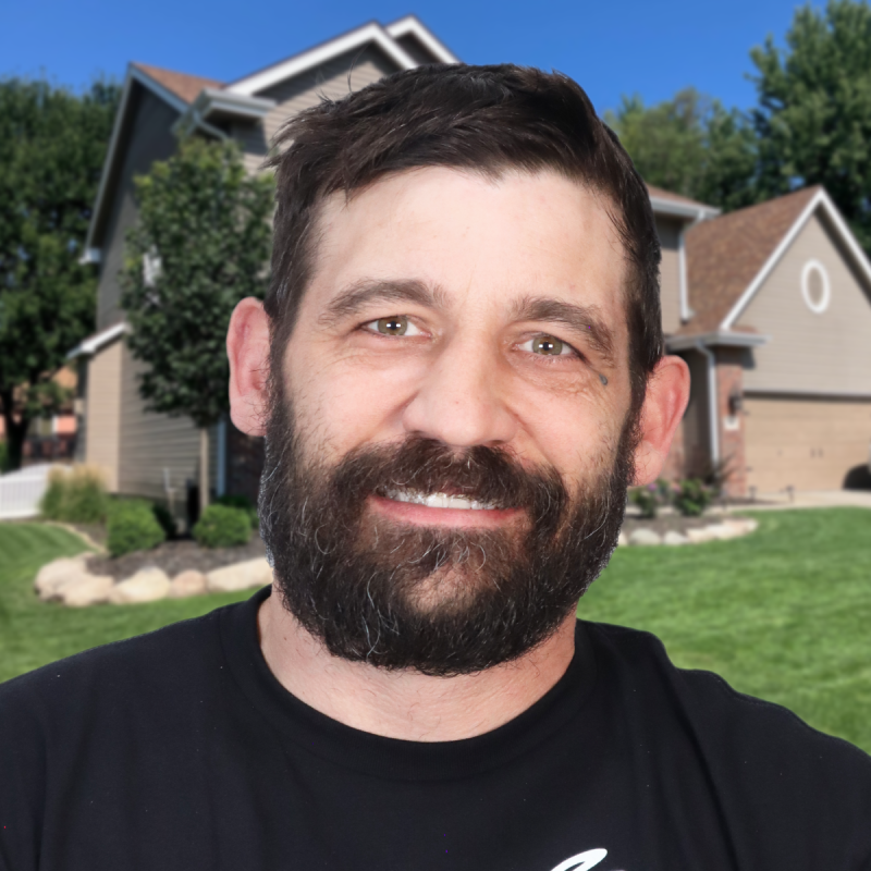 Smiling man standing in front of a suburban house on a sunny day.