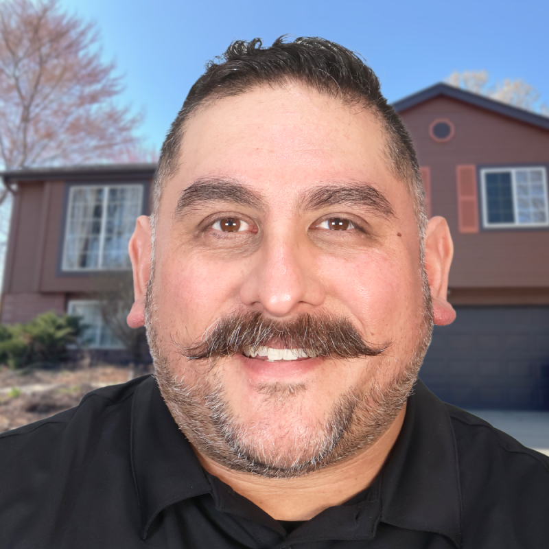 Smiling man with a mustache in front of a suburban home on a sunny day.