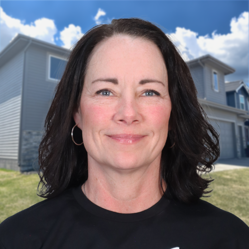 Smiling woman standing in front of a modern suburban home under a blue sky.