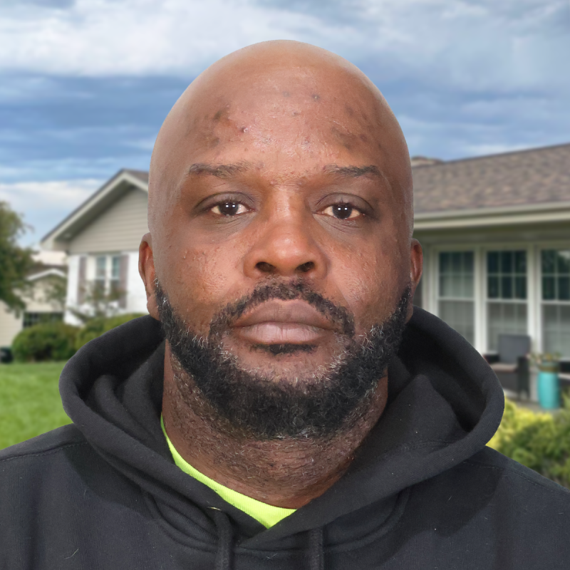 Man in a black hoodie stands in front of a suburban home with a shingled roof.