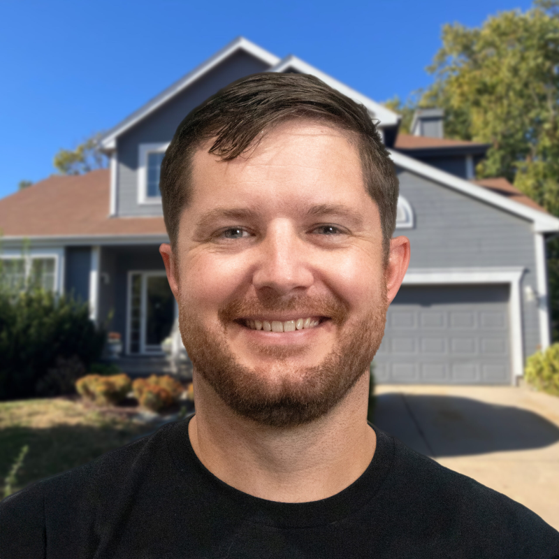 Smiling man standing in front of a suburban gray house with a garage.