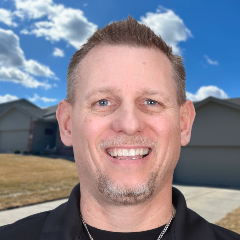 Smiling man stands outside residential home under a blue sky with clouds.