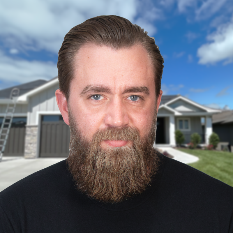 Man with a beard standing in front of a modern house under a blue sky.