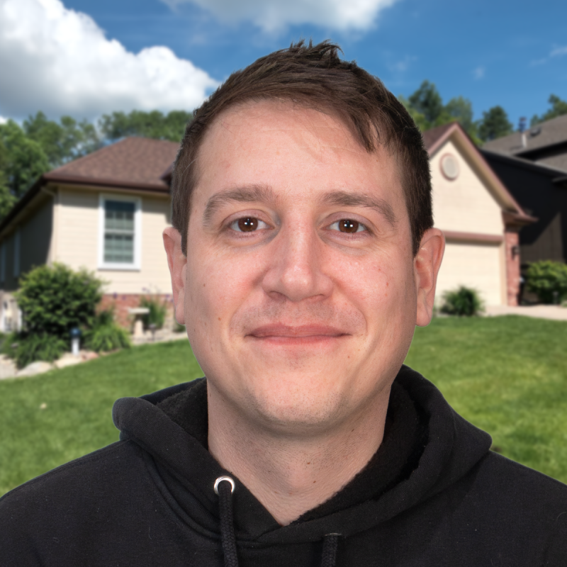 Man smiling in front of a suburban home with a well-kept lawn.