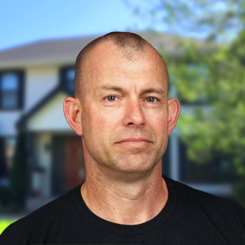 A man in a black shirt standing in front of a two-story house with trees.