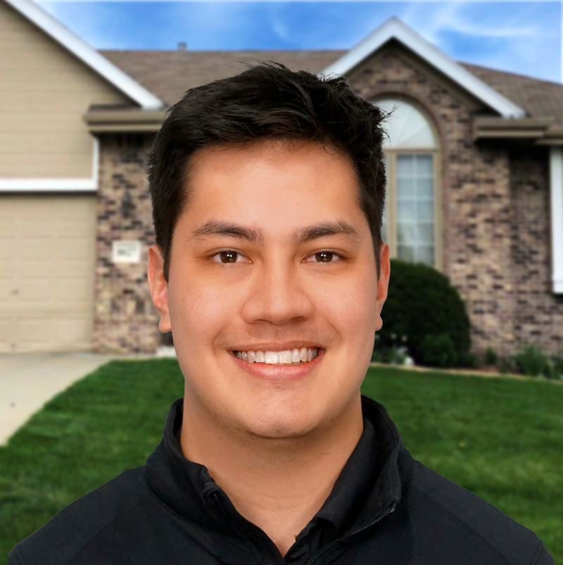 Smiling professional in front of a brick home under clear blue skies.