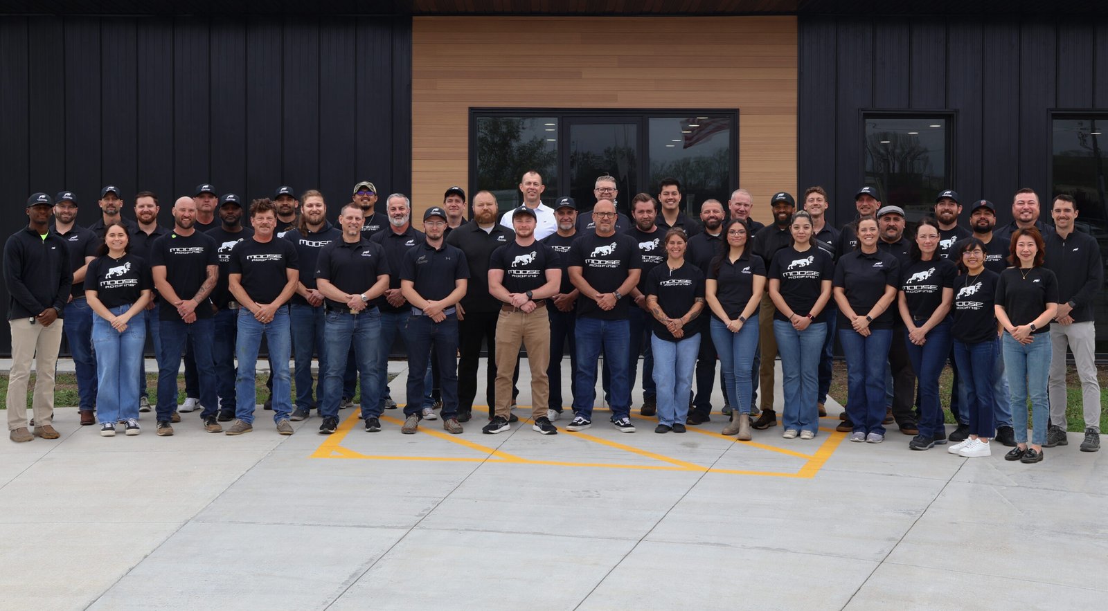 A roofing team poses for a group photo outside their company building.